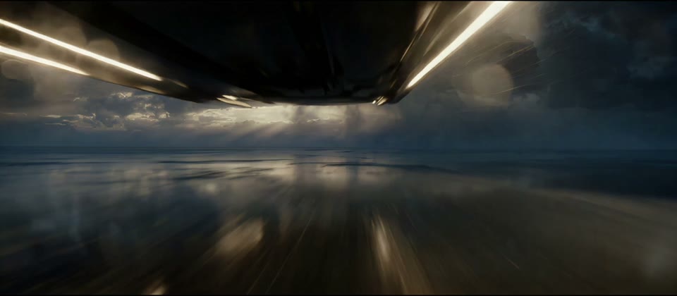 The underside of a silver train rushing across a reflective salt plain beneath a stormy sky