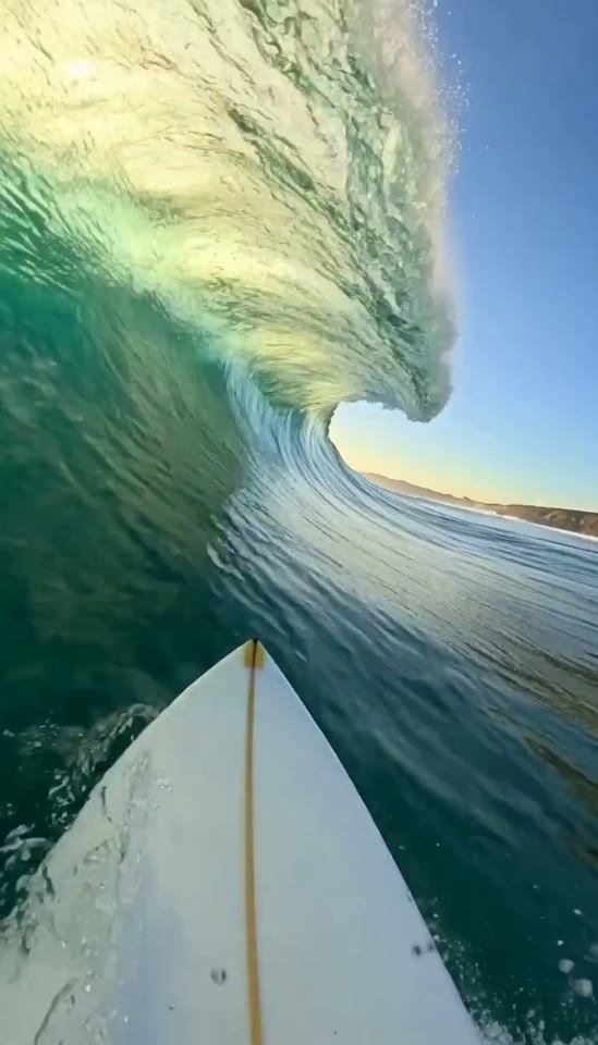 A first-person view from a surfboard inside a curling wave at sunrise